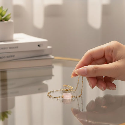 Hand hält ein spiritualsavagee Armband aus natürlichem rosa Quarz mit goldfarbenen Akzenten auf einem Glastisch.