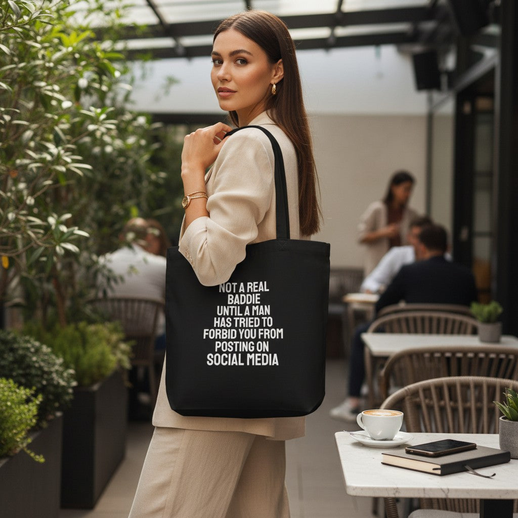 Frau trägt eine schwarze spiritualsavagee Bio-Baumwoll-Tragetasche mit weißem Statement-Aufdruck in einem Café.