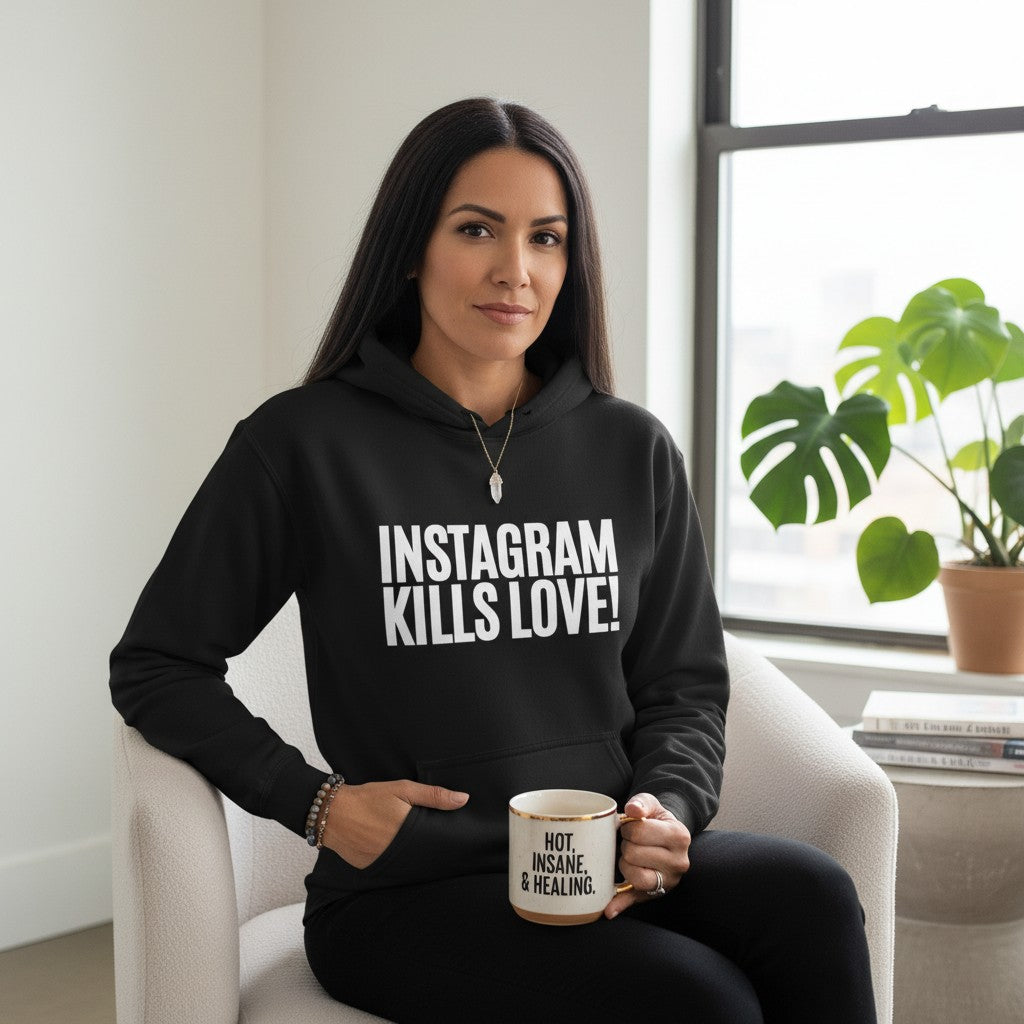 spiritualsavagee schwarzer Unisex-Hoodie mit weißem Instagram Kills Love Aufdruck, getragen von einer Frau im Sessel