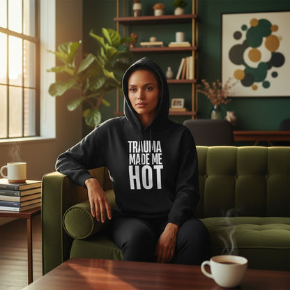 Eine Frau trägt den schwarzen spiritualsavagee Unisex-Hoodie mit dem weißen Schriftzug TRAUMA MADE ME HOT im Wohnzimmer.