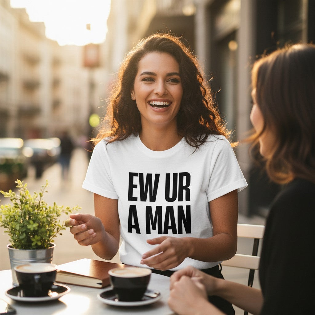 Eine Frau trägt ein weißes spiritualsavagee T-Shirt mit dem schwarzen Aufdruck EW UR A MAN in einem Café.